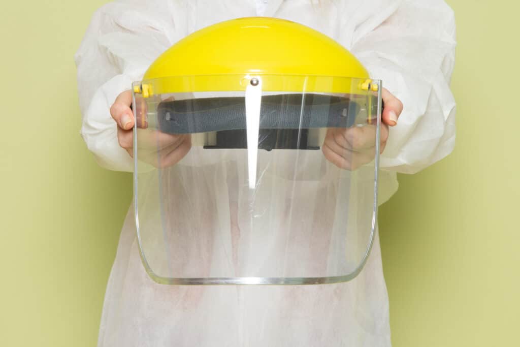 Person holding a yellow safety face shield for injury prevention.